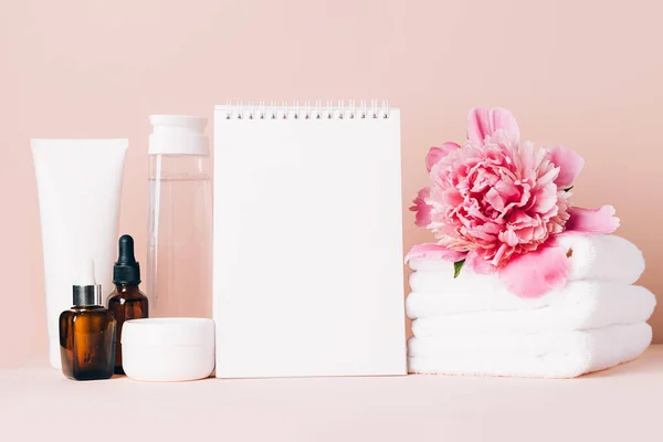 Los accesorios para mujer el aceite de crema los cosméticos distintos limpian el cuaderno en blanco sobre la mesa con las flores. Concepto de belleza — Foto de Stock