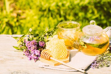 Yaz bitkilerinden taze yapraklar, yonca, kırsal bir arka planda cam çaydanlık kabında doğal sıvı bal peteği.