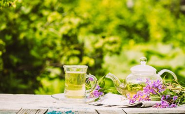 Taze limonlu çay, yaz bitkileri cam bardakta yonca yaprakları ve ahşap kırsal arka planda çaydanlık.