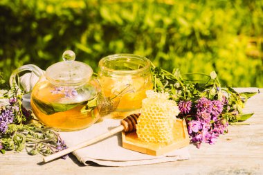 Yaz bitkilerinden taze yapraklar, yonca, kırsal bir arka planda cam çaydanlık kabında doğal sıvı bal peteği.