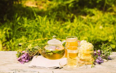 Taze limonlu çay, yaz bitkileri cam bardakta yonca yaprakları ve ahşap kırsal arka planda çaydanlık.