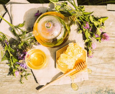 Yaz bitkilerinden taze yapraklar, yonca, kırsal bir arka planda cam çaydanlık kabında doğal sıvı bal peteği.