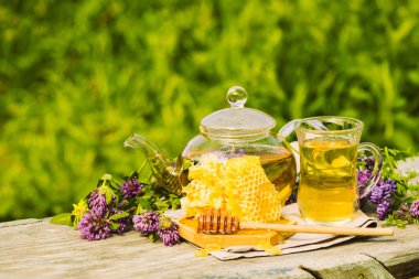 Yaz bitkilerinden taze yapraklar, yonca, kırsal bir arka planda cam çaydanlık kabında doğal sıvı bal peteği.
