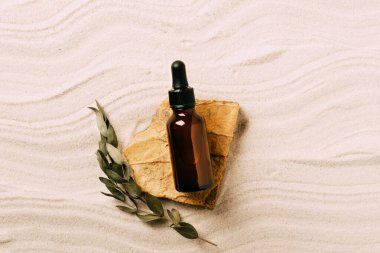 Kum arka planında serum kozmetik şişesi. Kumlu arka planda doğal malzeme ürün sunumundan soyut podyum. Üst görünüm kopyalama alanı.