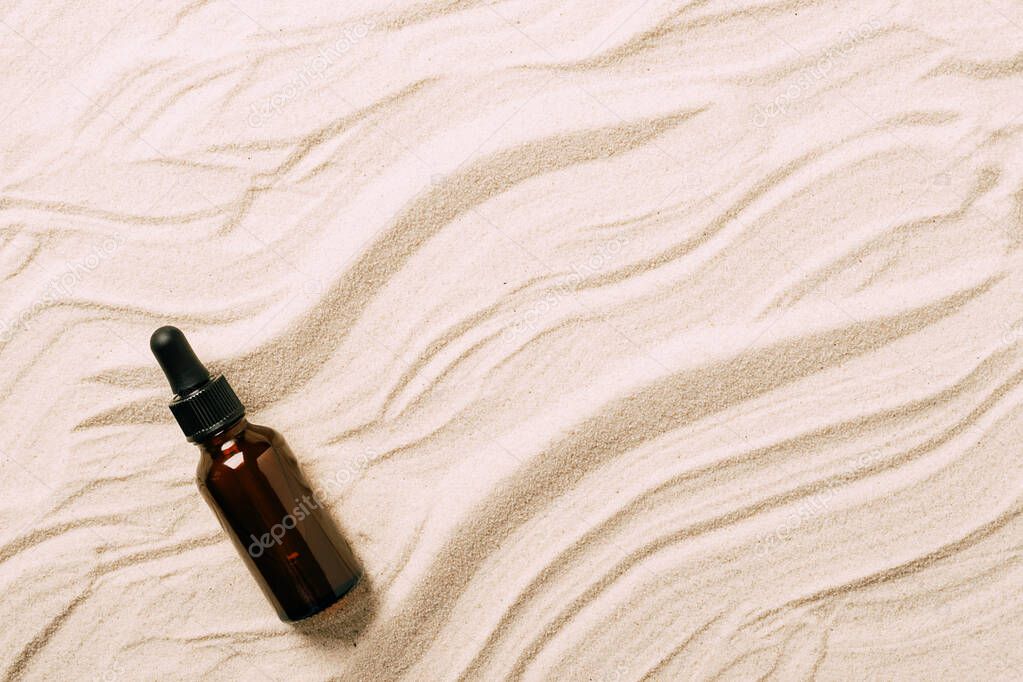 Bottle of serum oil cosmetic product beach sand background. Abstract podium product presentation on a sandy background