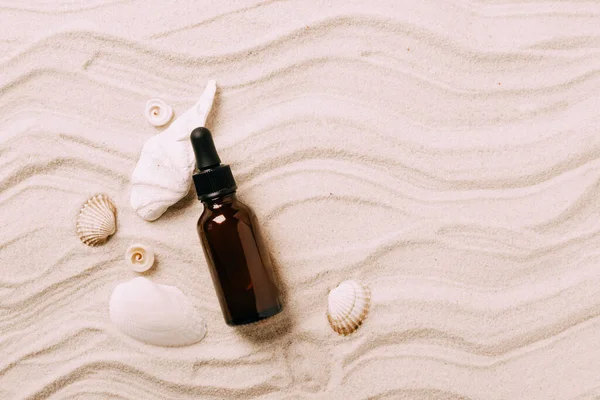 Botella de vidrio con suero de aceite esencial fondo del producto cosmético de conchas marinas arena de playa, presentación del producto — Foto de Stock