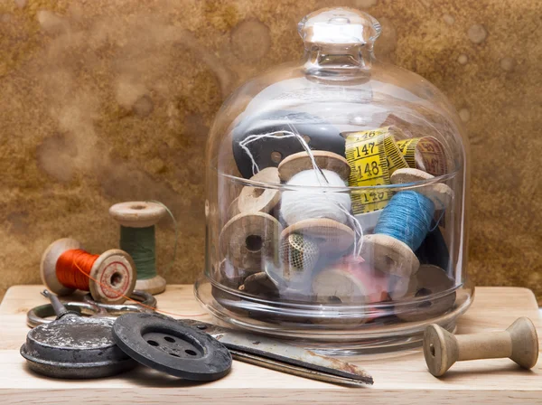 Spools of colored thread and tools for sewing in a glass vase , buttons, oiler  and needles on the wooden board — 스톡 사진