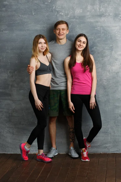 Three beautiful friends one man and two woman smiling in a gym