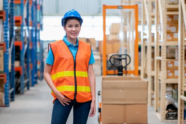 Portrait of warehouse woman or factory worker with blue hat and uniform stand in front of hand stacker or hydraulic cart in workplace. Concept of good management and in delivery industrial business.
