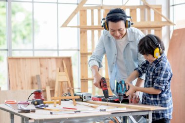 Ses kesen kulaklığı olan Asyalı bir baba oğluna elektrikli matkabı evlerinde ahşap işçiliğinde kullanmasını öğretiyor. Hobi ile iyi ilişki kavramı ya da mutlu aile aktiviteleri.