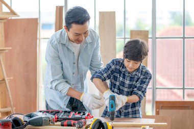 Asyalı bir baba oğluna evlerinde ahşap işçiliği için elektrikli matkap kullanmayı öğretiyor. Hobi ile iyi ilişki kavramı ya da mutlu aile aktiviteleri.