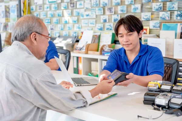 Customer service Asian worker or staff at office counter area receive credit card for payment from senior man. Concept of good service for customer support business system.