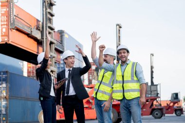 Kargo konteynırı çalışanları ya da bir grup işçi neşeli duygu ve eylemlerini ifade eder. İş yerinde başarılı bir şekilde kutlanır. Arka planda vinç ve nakliye konteyneri yığını bulunur..