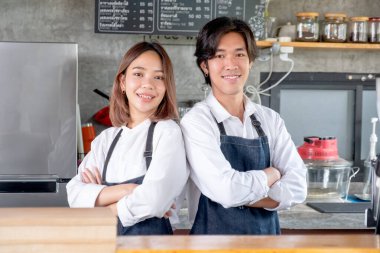 İki Asyalı barista ya da kahve makinesi kolları çapraz ya da kendine güvenen iki erkek ve kadın da kameraya bakar