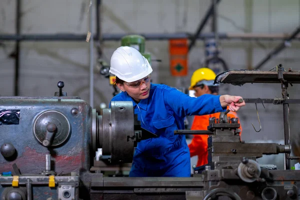 Factory worker woman or technician look to part of the machine and inspect the function while her co-worker work with other machine in the background.