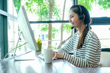 Asyalı kadın kulaklıklı bilgisayar kullanıyor. Yeni normal yaşam tarzıyla evde kaldığı süre boyunca internet üzerinden toplantı yapıyormuş gibi görünüyor..