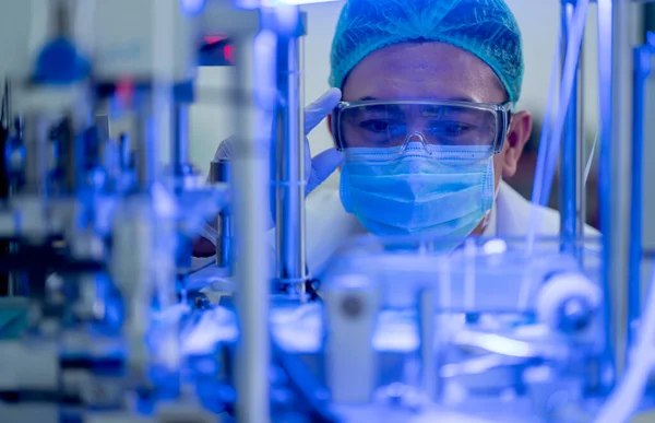 Close up face of factory worker touch protective eye glasses and look into part of machine with blue light. Concept of quality control in factory industry business.