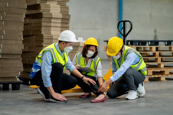 Two factory worker man help and take care coworker after accident on her leg by hydraulic cart in workplace. Concept of safety for employee in industrial warehouse business.