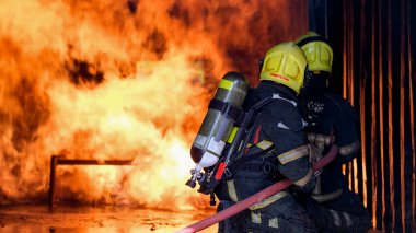 İki itfaiyeci yangın hortumuyla söndürmeye ya da söndürmeye yardım ediyor. İtfaiyecilerin takım çalışması kavramı insanlara yardım eder.