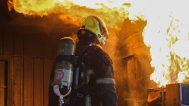 Koruyucu takım elbiseli itfaiyecinin arkası antrenman sırasında mutfak duvarındaki yangına bakın ya da hazırlık için personel alın ve profesyonel olarak çalışmaya hazır olun..