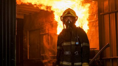 Koruyucu takım elbiseli itfaiyecinin portresi mutfaktaki ateşin önünde duruyor ve kameraya bakıyor. Ayrıca elinde baltayla yangını söndürmeye hazırlanıyor..
