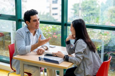 Yakın çekim İspanyol adam otur ve gündüz ışığıyla birlikte cam pencerenin önünde, halk kütüphanesindeki Asyalı kadınla konuş..