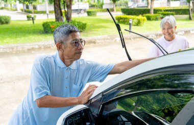 Asyalı son sınıf öğrencisi yaşlı kadınla arabasını temizlemek için araba havlusu kullanıyor ve evlerinin önünde mutluluğa bakıyor..