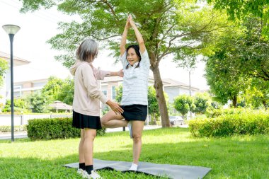 Asya 'lı son sınıf öğrencisi bir kadının ayakta durup, arkadaşının gündüz vakti yoga yapmasına yardım etmesi..