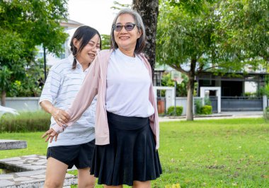 Asyalı son sınıf öğrencisi kadın ayağa kalkar ve arkadaşının kollarını ve omuzlarını gün ışığında bahçede esnetmesine yardım eder..