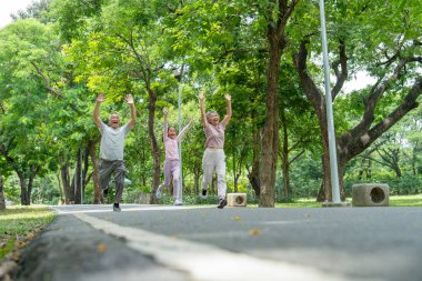 Kıdemli erkek ve kadının, kız kıza hareket halindeki geniş açılı görüntüleri. Kamu parkında birlikte koşarken yarışmayı kazanmak gibi ellerini kaldırıyorlar..