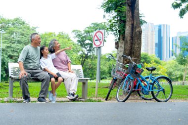 Asyalı büyükbaba ve büyükanne ya da kıdemli erkek ve kadın halk parkında bahçe bankında mutlulukla otururken kızın işaret ettiği yöne bakın..
