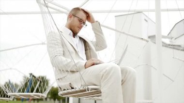 Salıncakta oturan dizüstü bilgisayarda çalışan adam