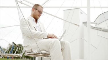 Salıncakta oturan dizüstü bilgisayarda çalışan adam