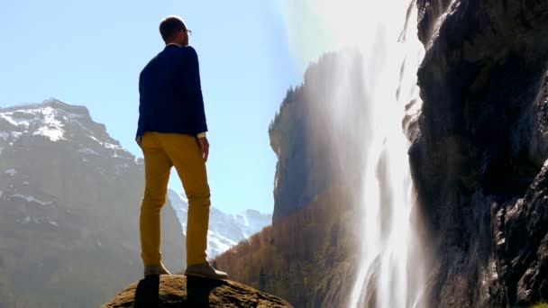 Homme debout sur un rocher de pierre et regardant la cascade . — Video