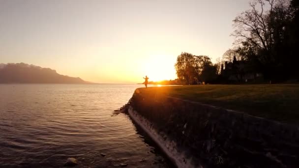 Man höjer armarna på stranden av sjön i solnedgången — Stockvideo