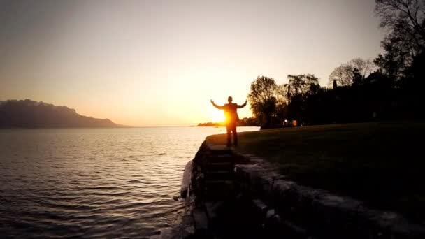 L'uomo alza le braccia sulla riva del lago al tramonto — Video Stock