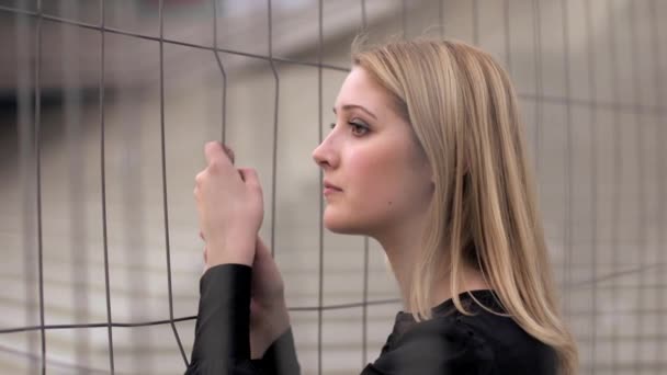Joven mujer triste vale la pena aferrarse a una valla de metal — Vídeos de Stock