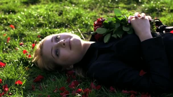 Молодая женщина лежит на зеленой траве и держит букет роз — стоковое видео