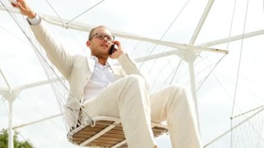 Adam salıncak üzerinde cep telefonuyla konuşuyor