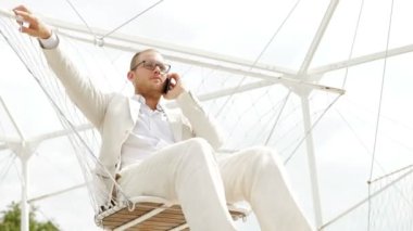 Adam salıncak üzerinde cep telefonuyla konuşuyor