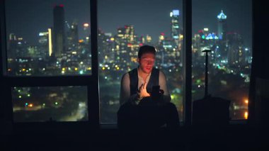 Bir adam, şehir ışıklarının pırıl pırıl parıltısıyla çevrili bir gökdelendeki yaşamı derin bir şekilde düşünür.