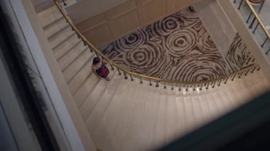 Zarif bir otel gelişi, Asyalı bir gezgin merdivenlerden iniyor, otelde gezgin ile sarmal merdivenler.