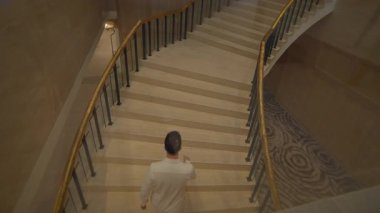 Lüks otelin gelişi, seçkin konuğumuz mermer merdivenlerden iniyor, lüks otel lobisinde dengeli bir şekilde.