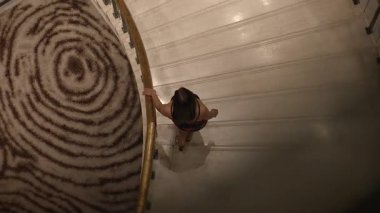 Güzel gelin zarif bir şekilde süslü halılar ve sıcak ışıklandırmayla süslenmiş sarmal merdivenlerden iniyor.