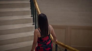 Kırmızı elbiseli zarif kadın merdivenlerden çıkıyor, kırmızı elbiseli kadın kıvrımlı otel merdivenlerine tırmanıyor.