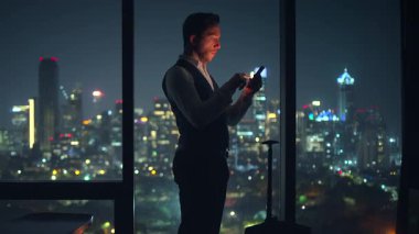 Bir iş adamı akıllı telefonuyla meşgul olurken çarpıcı bir şehir arkaplanına karşı duruyor.