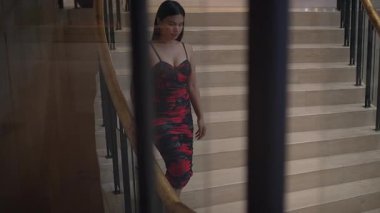 woman pausing on staircase with railings, asian woman gazing downward on curved staircase in hotel