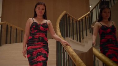 elegant asian model gracefully descending grand staircase with mirror reflection and warm lighting