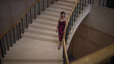 woman in red descends staircase, confident woman in red elegantly descends grand staircase at event