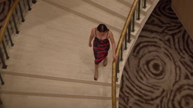 asian performer moves gracefully down spiral staircase adorned with dramatic carpet pattern